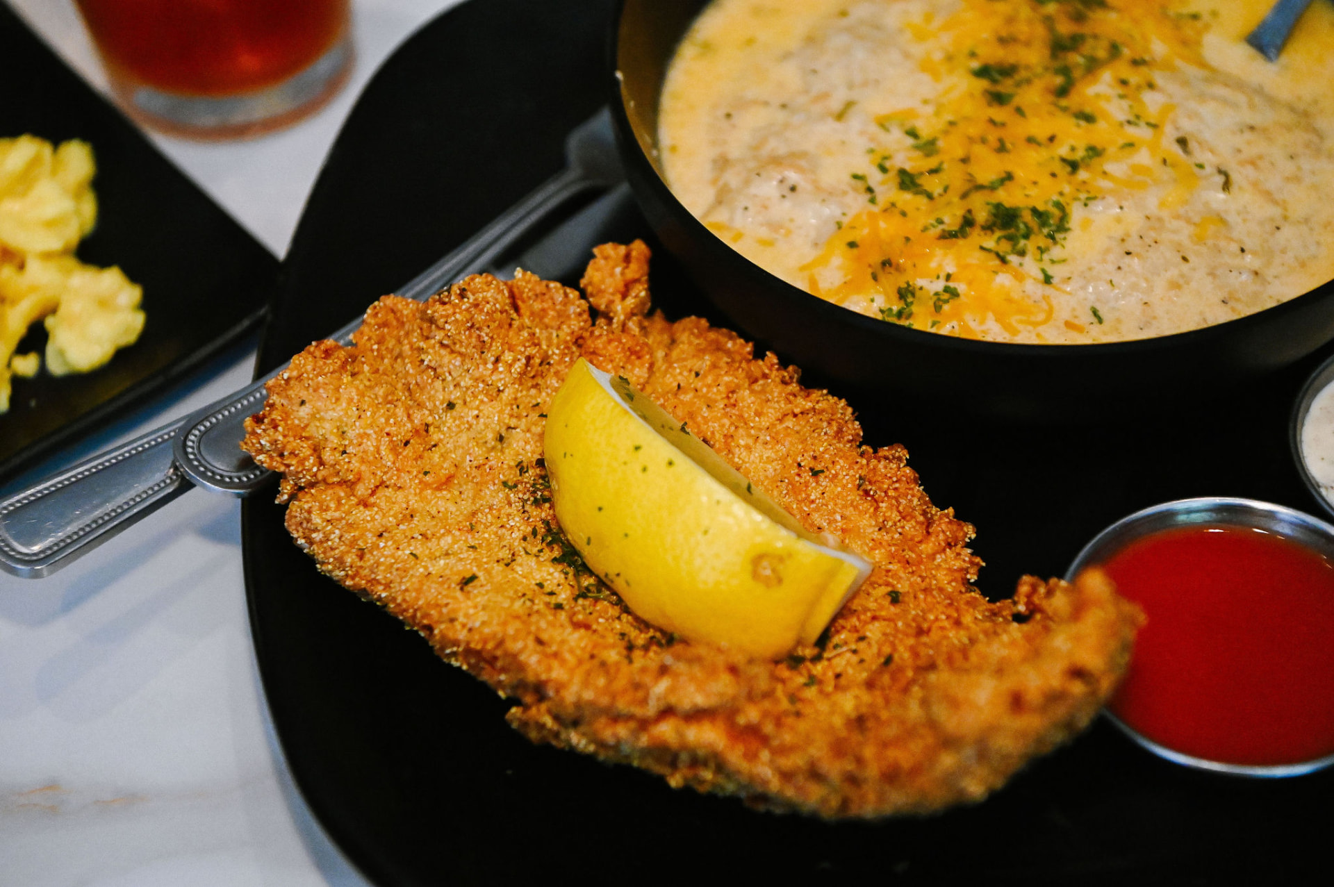 Gritz N Wafflez cornmeal-crusted fried fish with lemon beside a skillet of cheesy gritz